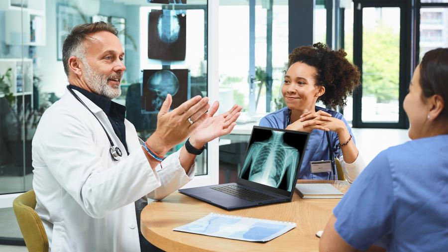 Lääkäri keskustelee kahden sairaanhoitajan kanssa. Hänen edessään pöydällä on ASUS ExpertBook -kannettava, jonka näytöllä näkyy röntgenkuva.