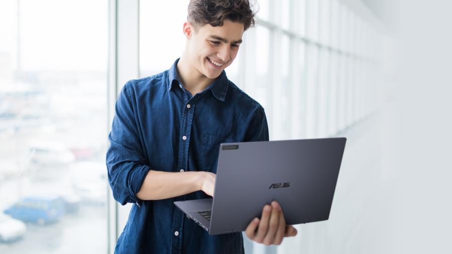 A man with a smile is holding an ASUS ExpertBook B5 in laptop mode with one hand while another typing. 