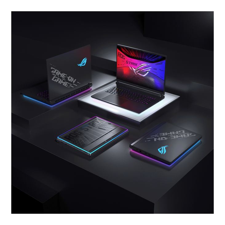 Four ASUS ROG gaming laptops displayed on a black platform with colorful lighting effects