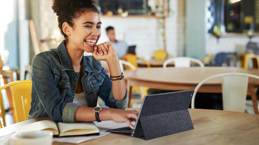 Leveästi hymyilevä nainen osallistuu videoneuvotteluun kahvilasta käsin ASUS ExpertBook -tietokoneellaan.