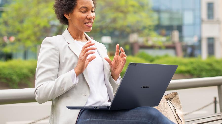 An african woman is sitting on a chair outdoor while having an ASUS ExpertBook B5 Flip in laptop mode on her lap. 