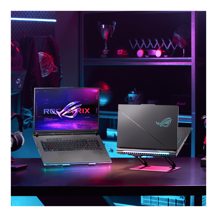 A dark room with purple lighting, with a desk featuring two Strix SCAR laptops, an OMNI figurine, and an ROG headset