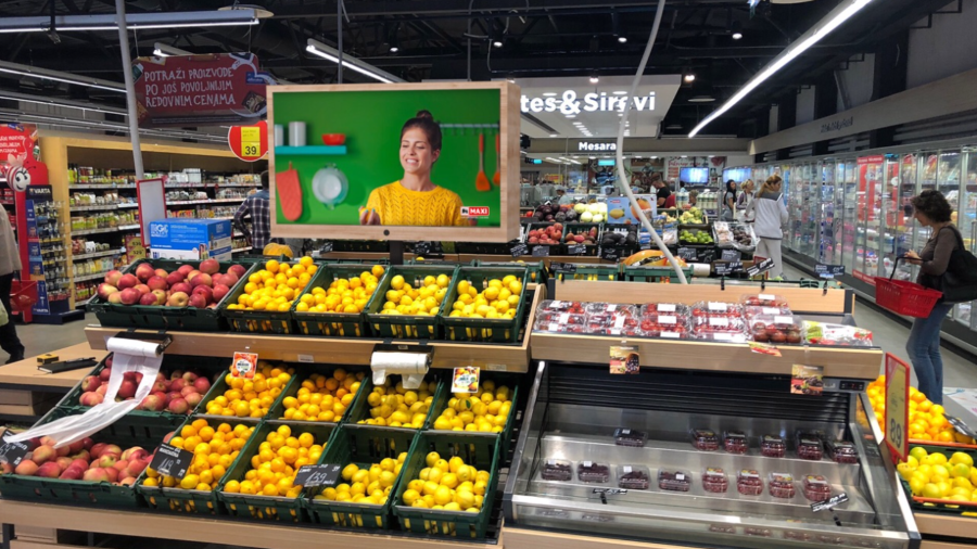 A digital signage display targeted ads in the fruit section of a grocery store