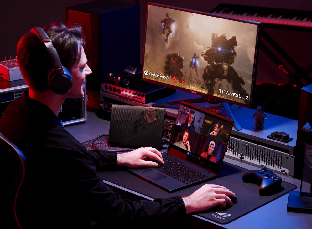 Gamer sitting at a desk with audio equipment, a Flow X13, XG mobile, and Titanfall 2 on an external monitor.