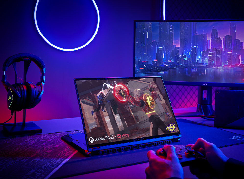 Gamer at a desk with a monitor, headset, and flow X16 in stand mode, playing a game with a controller.
