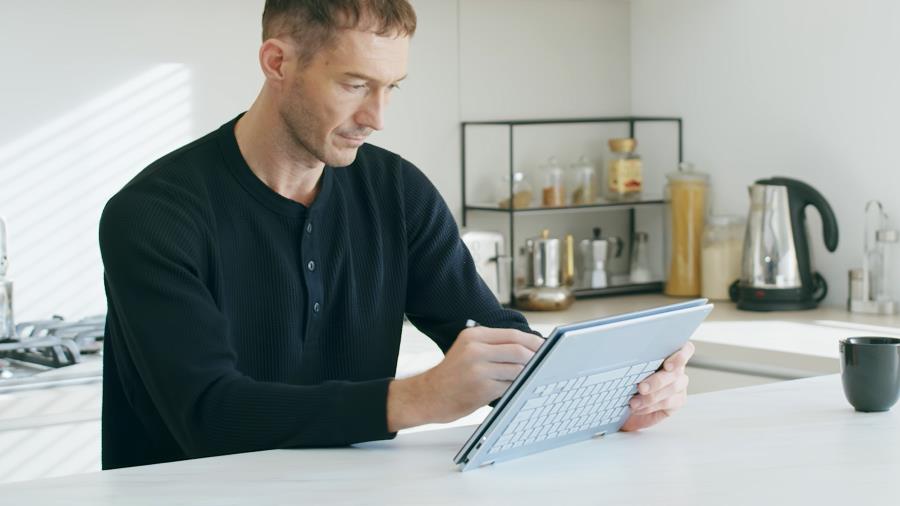 Podnikatel v kuchyni pracuje na svém notebooku ASUS Chromebook se stylusem v ruce.