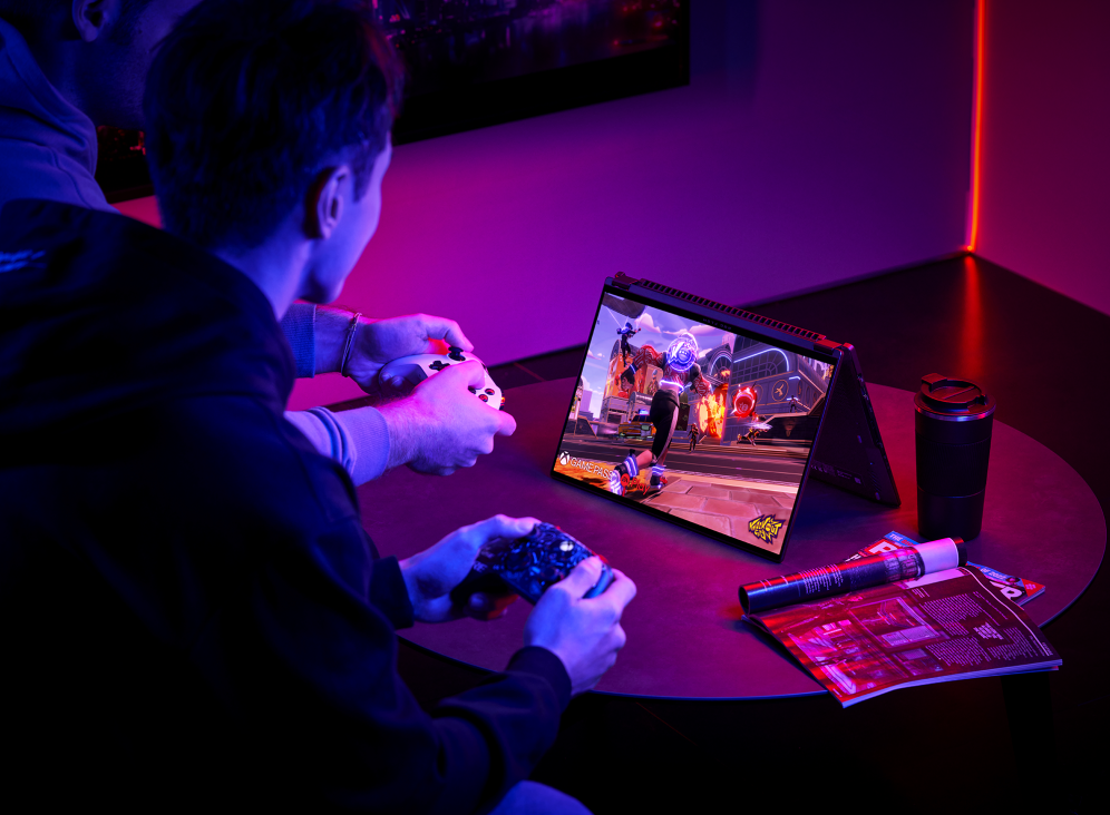 Two gamers playing on controller, with a Flow X16 in tent mode on a coffee table.