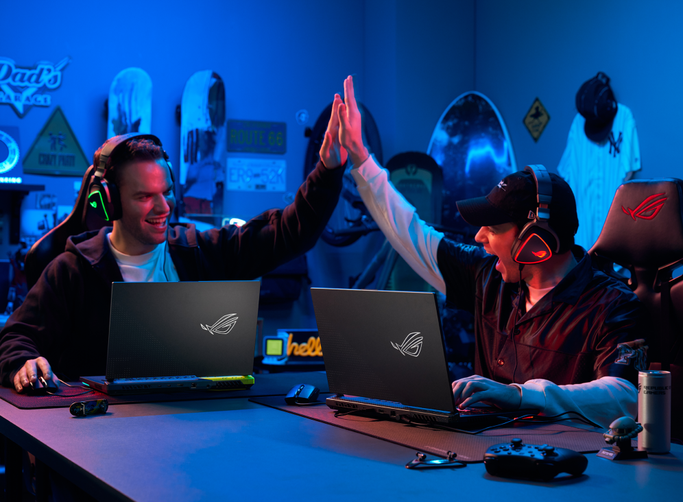 Two people sitting at a table, both with a Strix G17, high-fiving.