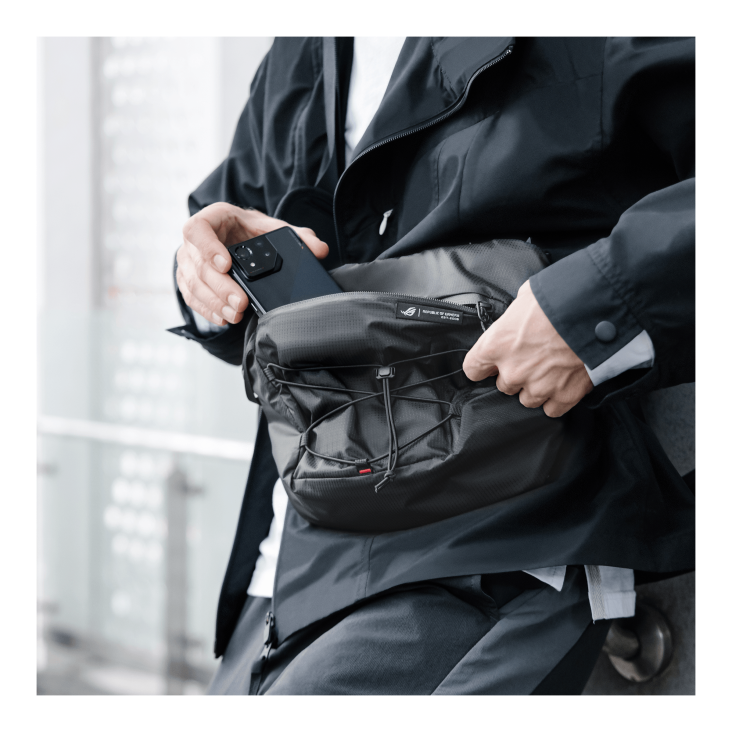 Person in a black suit taking a smartphone out of a shoulder bag outdoors