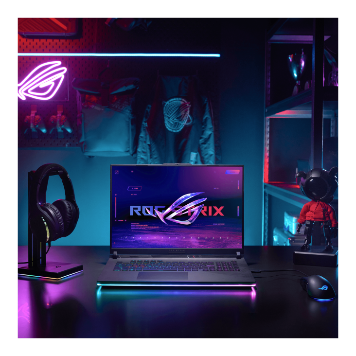 A dark room with purple lighting, with an ROG neon sign, and a desk featuring the ROG Strix SCAR laptop, an ROG headset, mouse, and OMNI figurine