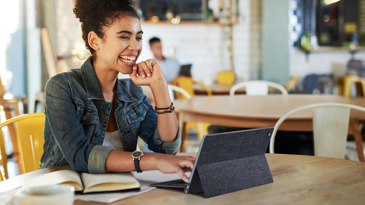 Eine Frau mit einem breiten Lächeln hält eine Videokonferenz mit dem ASUS ExpertBook abnehmbaren Laptop in einem Café ab.