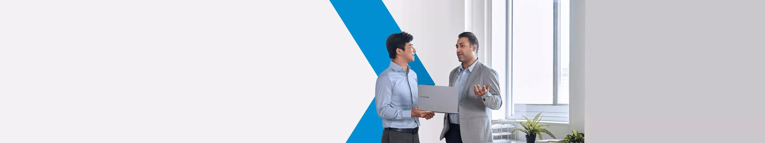 Man holding laptop speaking to coworker