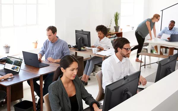 Seven people working on ASUS ExpertBooks and ASUS ExpertCenters in a white office with brown wooden tables.