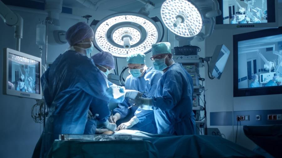 在手術室裡，一位醫生與三位醫療人員一起進行同步操作，周圍有三個屏幕。