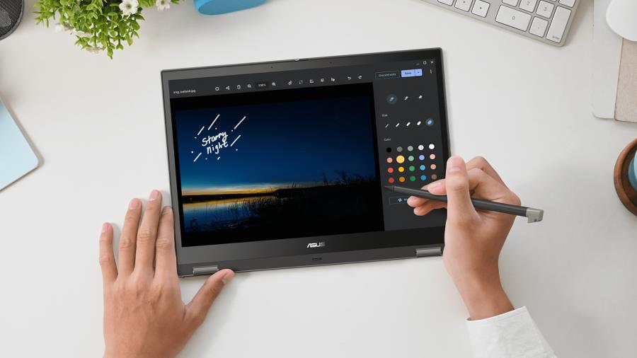 A person's hands using a stylus on an ASUS  Chromebook CM34 Flip tablet. The person is drawing a landscape image with a blue sky and a sunset over a lake. 