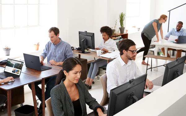 Sept personnes travaillant sur des ExpertBooks et des ExpertCenters d’ASUS dans un bureau blanc avec des tables en bois marron.