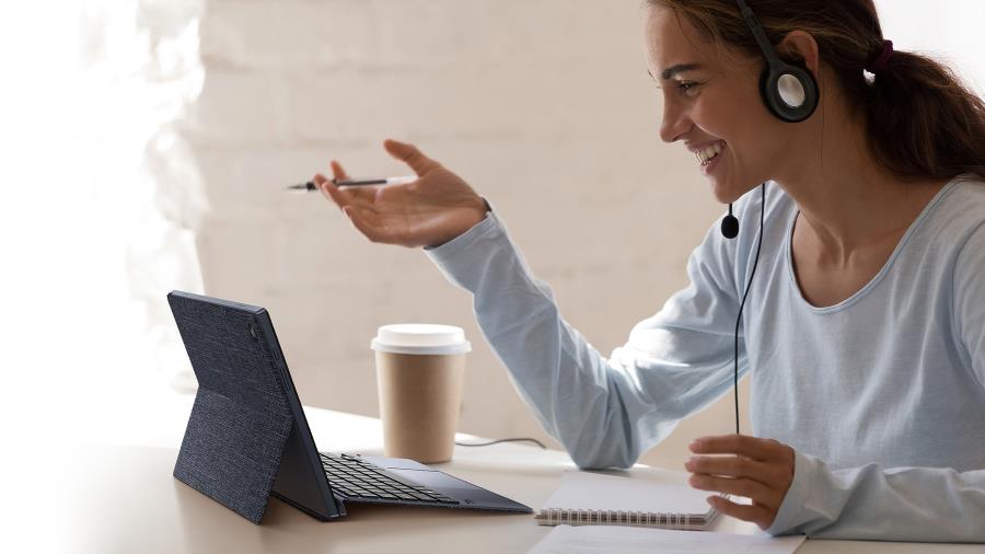 A woman with a smile wears earphones and a microphone while using an ASUS ExpertBook B3 Detachable with both ASUS ExpertStand and ASUS ExpertBoard peripherals attached in front of him. 