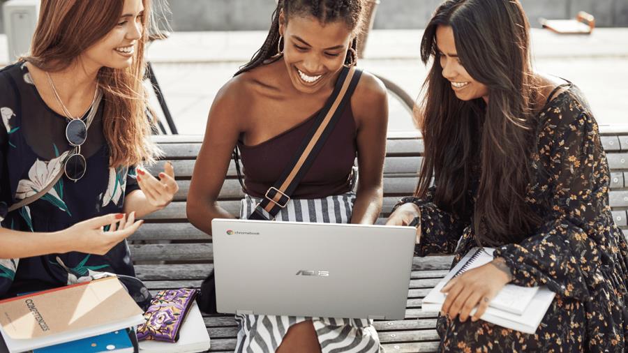 Three women are sitting on the bench while the woman in the middle is having an ASUS Chromebook CX1 on her lap. 